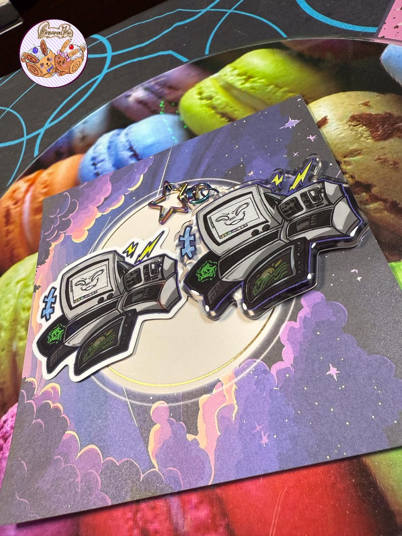 May include: Two enamel pins with a retro computer design, a smiling face on the screen, lightning bolts, and a star. The pins are set against a backdrop of a purple and blue night sky with clouds.