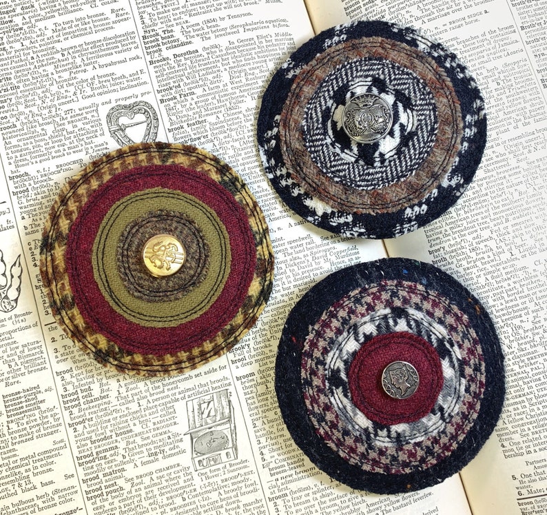 May include: Three circular fabric coasters with different patterns and colors. Each coaster has a button in the center. The coasters are made of a variety of fabrics, including plaid, tweed, and houndstooth.