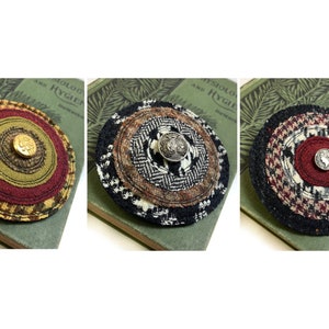 May include: Three round fabric brooches with different patterns and colors. Each brooch has a button in the center. The brooches are on a green book with text that says "Physiology and Hygiene".
