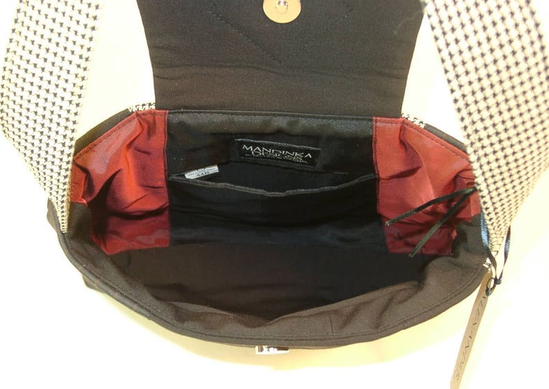 May include: Black shoulder bag with a flap closure, featuring a black and white patterned strap. The interior is black with red accents and multiple pockets. The bag has a metal clasp and a gold-colored button.