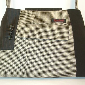 May include: A rectangular tote bag made from repurposed suit materials. The bag features a houndstooth pattern, pinstriped fabric, and black accents. It has a pocket with a label and buttons on the side. The bag has a shoulder strap.