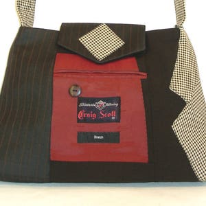 May include: A unique shoulder bag crafted from repurposed suit fabrics. The bag features a black and brown pinstripe pattern, a red pocket with a button, and a houndstooth flap. The label reads "Craig Scott" and "Stretch".