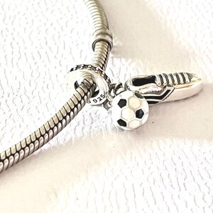 Puede incluir: Pulsera de plata con un charm de plata que representa un balón de fútbol y una bota de fútbol.
