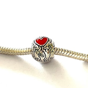 Puede incluir: Abalorio de plata con un coraz&oacute;n de esmalte rojo en una pulsera de cadena de serpiente de plata.