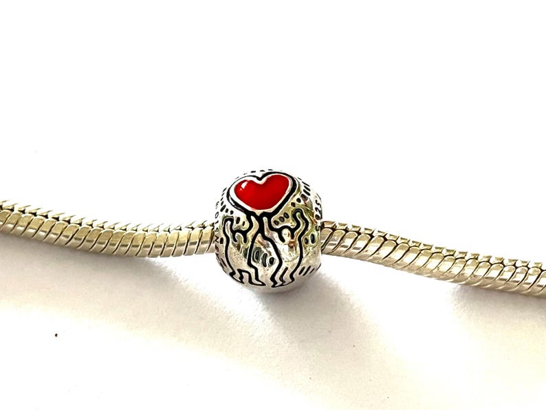 Puede incluir: Abalorio de plata con un coraz&oacute;n de esmalte rojo en una pulsera de cadena de serpiente de plata.