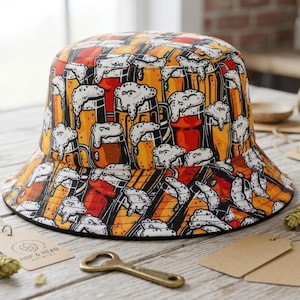 Może przedstawiać: Czapka typu bucket hat z powtarzającym się nadrukiem graficznym przedstawiającym kufle piwa wypełnione złotym płynem i białą pianą. Wzór ukazuje różne szklanki do piwa w odcieniach pomarańczu, żółci i czerwieni z grubymi czarnymi konturami.
