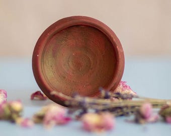 May include: A small, round, terracotta-colored ceramic bowl with a textured interior. The bowl is surrounded by dried lavender and pink rose petals, creating a natural and rustic aesthetic. The bowl is likely used for decorative purposes.