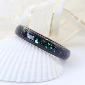 May include: A black ring with a thin band of iridescent green and blue glitter embedded in the resin.