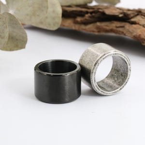 Op de afbeelding: Twee ringen, een zwarte en een zilveren, met een verweerde, verweerde afwerking. De ringen zijn dik en hebben een afgeronde vorm.