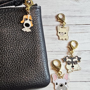 May include: Dog-themed charm collection featuring four different dog breeds. Each charm is made of gold-colored metal and enamel, with a lobster clasp for easy attachment. The charms are attached to a black leather wallet.