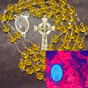 Peut inclure: Un chapelet en verre jaune avec une croix celtique dorée et un petit pendentif ovale représentant une femme. Le chapelet brille d'une couleur rose vif sous une lumière noire.