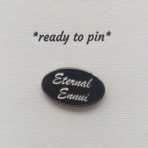 May include: Black enamel pin with white text that reads "Eternal Ennui".