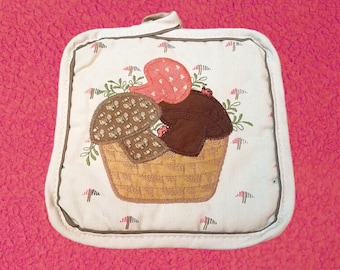 May include: A white pot holder with a brown, beige, and red mushroom design. The mushrooms are in a basket with green leaves and red ladybugs.