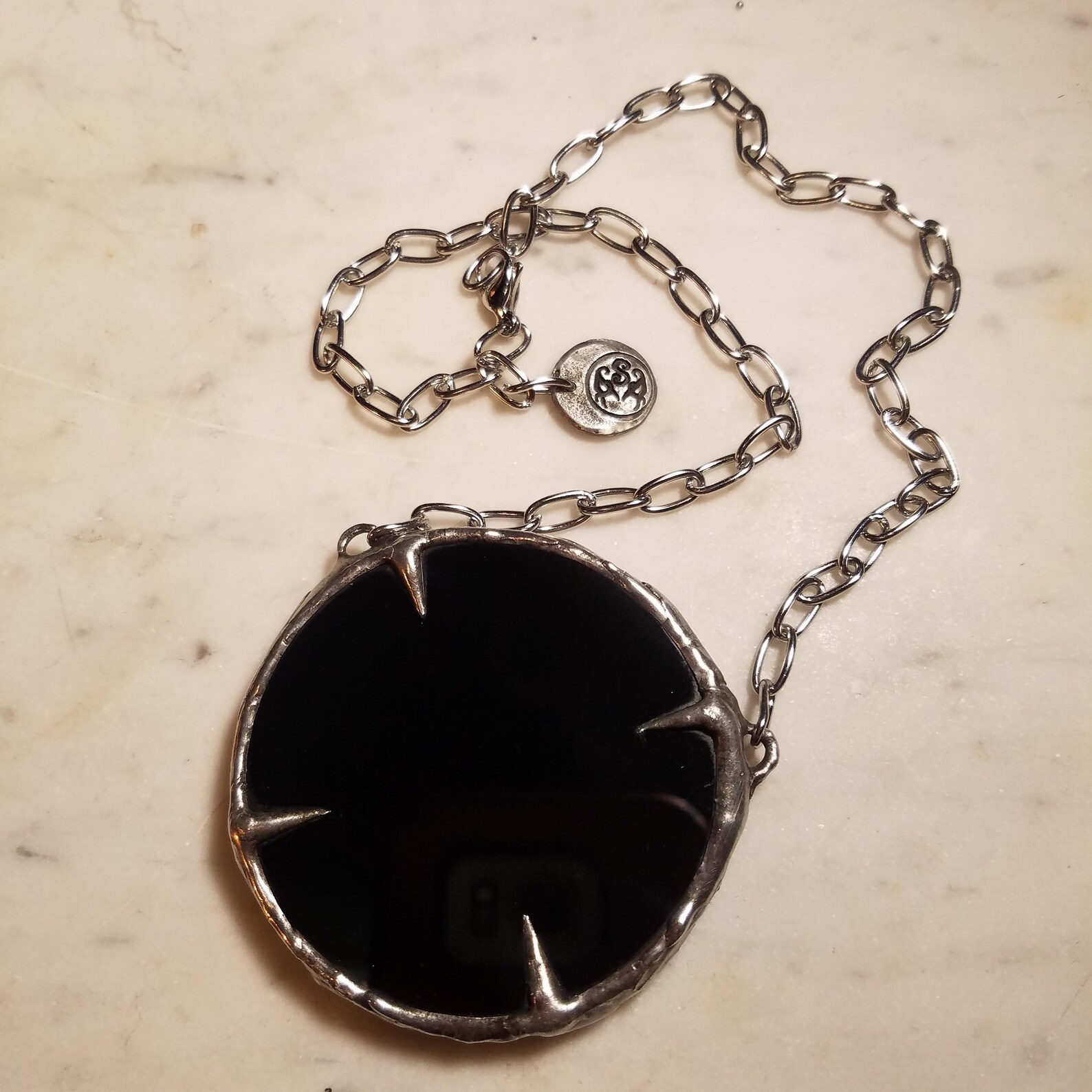Large black obsidian pendant with silver talon setting on chain, shown on marble background