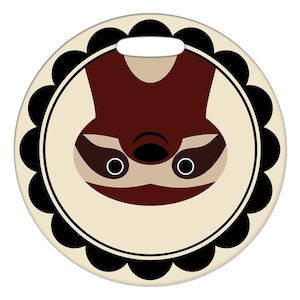 Puede incluir: Una etiqueta de equipaje redonda con un borde festoneado blanco y negro. Dentro del borde, un fondo beige con una cara de perezoso marrón mirando hacia abajo.