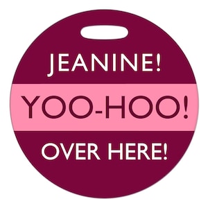 May include: A round, burgundy luggage tag with a pink stripe and white text that reads "Jeanine! Yoo-hoo! Over here!"