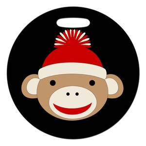 May include: A round black luggage tag with a cartoon monkey wearing a red and white knit hat with a white pom-pom.