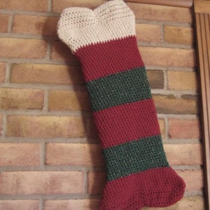 May include: A crocheted Christmas stocking with red, white, and green stripes hanging on a brick wall.