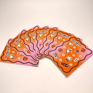 May include: A stack of square stickers with a pink and orange gradient background. Each sticker features Garfield characters and the text "SQUAWKEY LEAKS". Various cartoon illustrations are scattered across the orange surface.