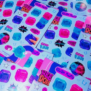 Könnte beinhalten: Mehrere Bögen mit Nee Doh Aufklebern in leuchtendem Pink und Blau mit quadratischen Formen. Die Aufkleber enthalten Texte wie SQUISH AWAY, GOOD VIBES, SO SATISFYING und SQUEEZE STRETCH CHILL sowie kleine Sterne, Smileys und Schmetterlingssymbole.
