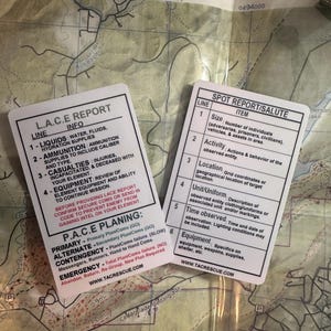 May include: A close-up of a laminated card with the acronym L.A.C.E. and the words "Report Info" printed on it. The card lists four categories: Liquids, Ammunition, Casualties, and Equipment. Below the L.A.C.E. report is a section titled "P.A.C.E. Planning" with the words "Primary, Alternate, Contingency, Emergency" printed on it. The card also includes the website address www.tacrescue.com.