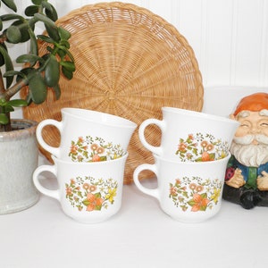 May include: Set of four white ceramic mugs with a floral pattern in shades of orange, yellow, and green. The mugs have a rounded shape and a handle on the side.