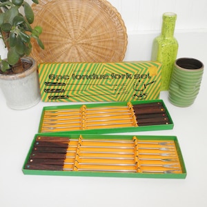 May include: A set of six fondue forks in a green and yellow box. The box has the text "6pc fondue fork set" printed on it. The forks have wooden handles with colorful dots and metal prongs.