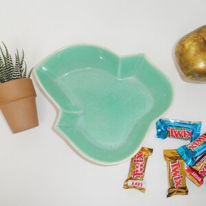 May include: A teal green ceramic leaf-shaped dish with a variety of Twix candy bars in blue and gold wrappers. The candy bars have the words "Twix", "Left", "Right", "Cookie Crisp", and "White Chocolate" printed on them.