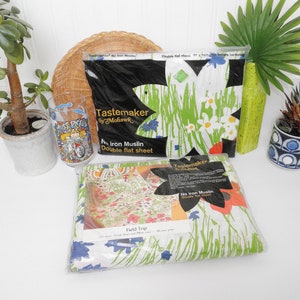 May include: Two packages of Tastemaker No Iron Muslin double flat sheets. The first sheet features a green and white floral pattern with blue accents. The second sheet features a green and white floral pattern with red accents. Both packages have the text "Tastemaker by Mohawk" and "No Iron Muslin Double Flat Sheet" printed on them.