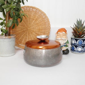 May include: A silver and copper pot with a lid and two handles. The pot has a speckled finish and the lid has a small, round knob.