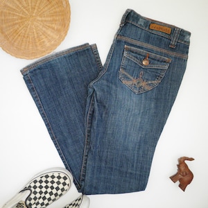 May include: A pair of blue denim jeans with a brown leather patch that says "Mudd" on the back waistband. The jeans have a light wash and a bootcut style.