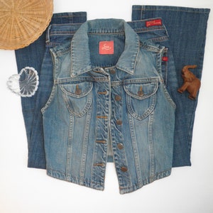 Pode incluir: Um colete de ganga azul com fecho de bot&otilde;es e dois bolsos frontais. O colete tem uma etiqueta Levi's na frente.