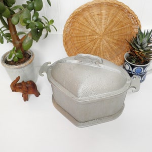 May include: A silver aluminum roaster with a lid and two handles. The roaster is hexagonal in shape and has a textured surface.
