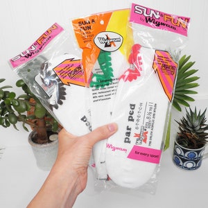 May include: Three pairs of white socks with colorful trim. The socks are packaged in clear plastic bags with pink, orange, and green branding. The packaging includes the text "Sun & Fun" and "Wigwam".
