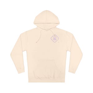 Peut inclure: Un sweat à capuche de couleur crème avec une poche kangourou sur le devant et des manches longues. Sur la poitrine supérieure gauche, un motif en forme de losange à bordure violet clair porte le texte Warning Night Fishing.