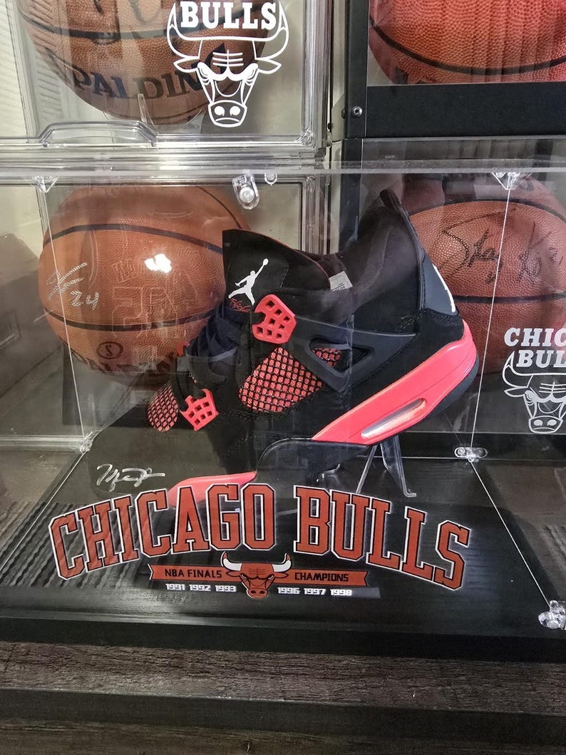 May include: A black and red Air Jordan basketball shoe with a clear display case. The case has a Chicago Bulls logo and the text "NBA Finals Champions 1991 1992 1993 1996 1997 1998".