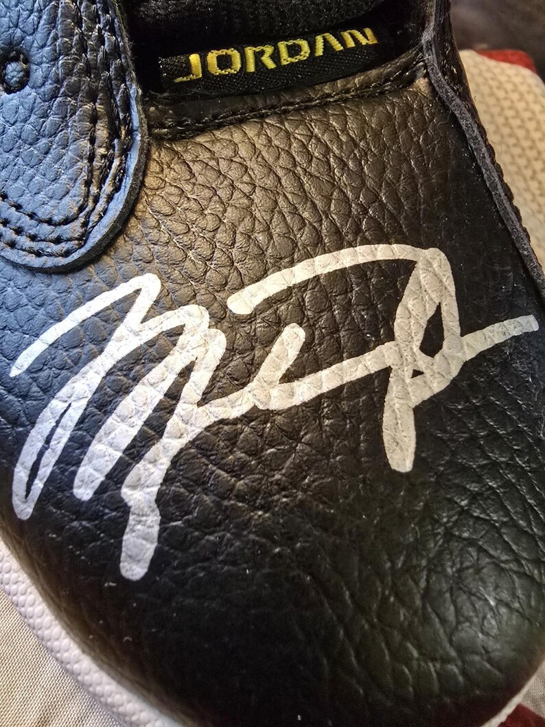 May include: Black leather shoe with a white signature that says "Mike" on the toe. The shoe has a gold "JORDAN" label on the top.