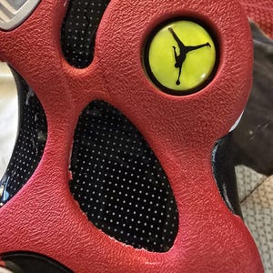 May include: Close-up of a red and black basketball shoe with a yellow Jumpman logo on the side. The shoe has a textured upper and a white sole.