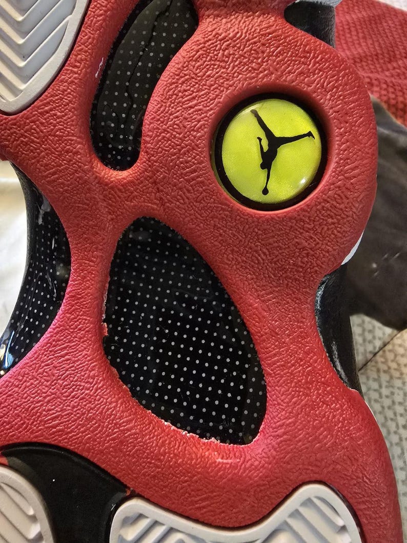 May include: Close-up of a red and black basketball shoe with a yellow Jumpman logo on the side. The shoe has a textured upper and a white sole.