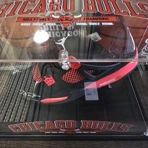 May include: A black and red basketball shoe in a clear display case with a Chicago Bulls logo and the text "NBA Finals 1991 1992 1993 Champions 1996 1997 1998"