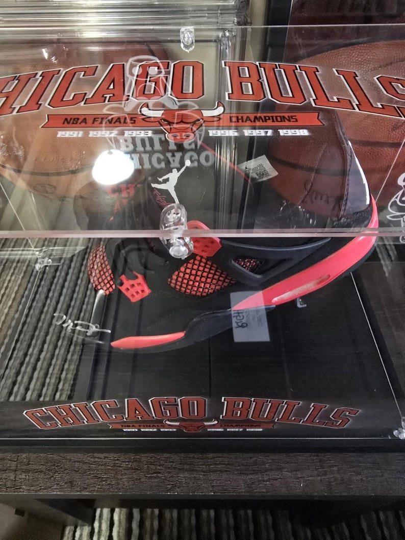 May include: A black and red basketball shoe in a clear display case with a Chicago Bulls logo and the text "NBA Finals 1991 1992 1993 Champions 1996 1997 1998"
