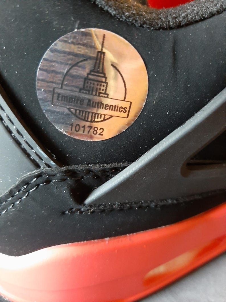 May include: A close-up of a black and red sneaker with a silver sticker that says "Empire Authentics" and the number "101782".