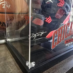 May include: A black and red basketball shoe with a red and white signature on the side. The shoe is in a clear display case with a black base. The shoe is labeled "Chicago" and "NBA Finals 1991".