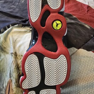 May include: The bottom of a black and red basketball shoe with a white tread pattern. The shoe has a yellow Jumpman logo on the heel.