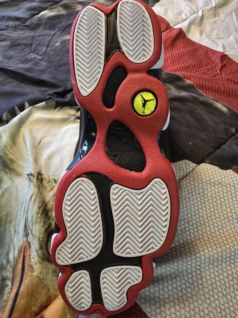 May include: The bottom of a black and red basketball shoe with a white tread pattern. The shoe has a yellow Jumpman logo on the heel.
