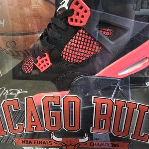 May include: Black and red Air Jordan basketball shoes in a display case with a basketball and the text "Chicago Bulls" and "NBA Finals 1991 1992 1993 Champions 1996 1997 1998".