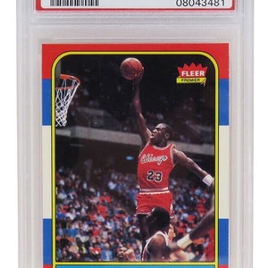 Könnte beinhalten: Eine Michael Jordan Basketballkarte von 1986 Fleer Premier, bewertet mit NM-MT 8 von PSA. Die Karte zeigt ein Foto von Jordan in einem rot-weißen Trikot der Chicago Bulls, der zum Dunk springt. Die Kartennummer ist #57.