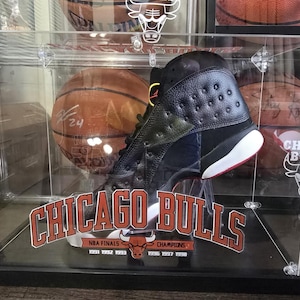 May include: A black and green basketball shoe with a red and white sole is displayed in a clear acrylic case with a basketball and the text "CHICAGO BULLS" and "NBA FINALS 1991 1992 1993 1996 1997 1998 CHAMPIONS".