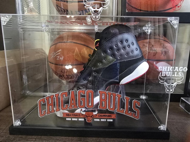 May include: A black and green basketball shoe with a red and white sole is displayed in a clear acrylic case with a basketball and the text "CHICAGO BULLS" and "NBA FINALS 1991 1992 1993 1996 1997 1998 CHAMPIONS".