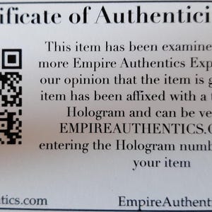 May include: A white certificate of authenticity with a black and white QR code in the upper left corner. The text reads "Certificate of Authenticity" and "This item has been examined by one or more Empire Authentics Experts and it is our opinion that the item is genuine. The item has been affixed with a tamperproof Hologram and can be verified at EMPIREAUTHENTICS.COM and entering the Hologram number affixed to your item." The bottom of the certificate reads "EmpireAuthentics.com" and "EmpireAuthentics@aol.com".